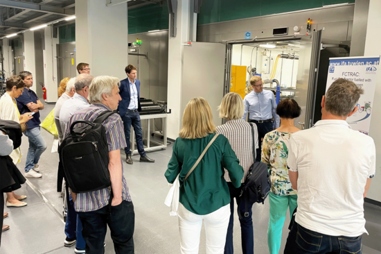 Gruppe von Besucher_innen hört einem Mann im Science Center der TUW zu. Rückenansicht.