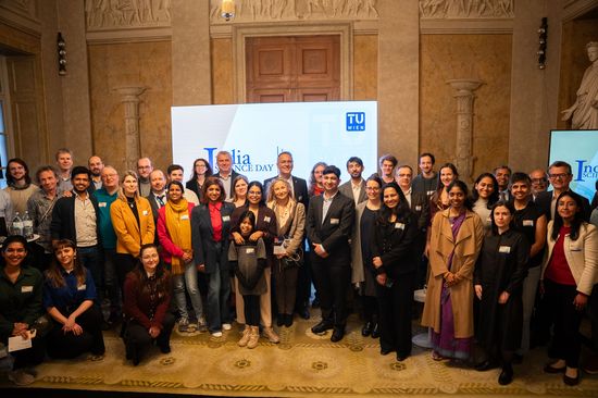 Gruppenfoto im Festsaal der TU Wien. Im Hintergrund sieht man ein großes Rollup. 