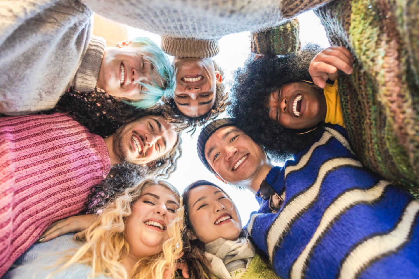 Seven young people stand in a circle and look down into the camera