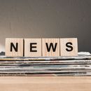 Four wooden blocks with the word NEWS printed on them are standing on a stack of newspapers. 