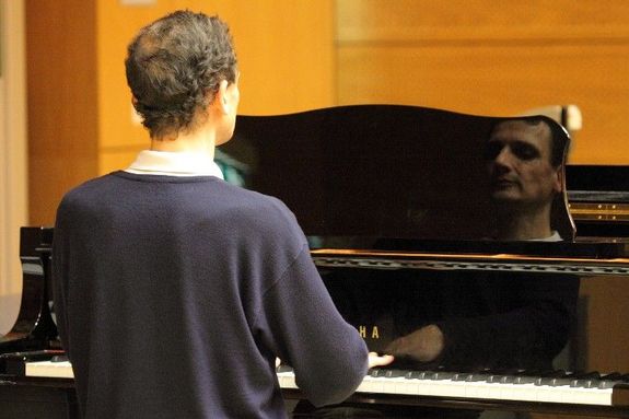 Mann am Klavier von hinten, Gesicht im Klavier gespiegelt