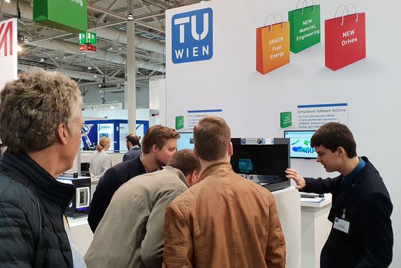 3 visitors get let themselves explain the NGSolve software based on a simulation shown at a hologram pyramid