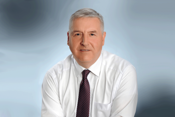 Porträtbild in Farbe mit blaugrauem Hintergrund.