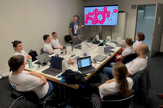 Neun Personen mit Laptops rund um einen Tisch