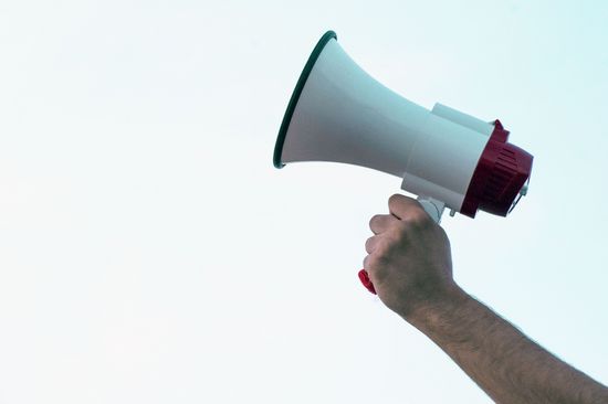 Megaphon von Hand in die Luft gerichtet vor blauem Himmel