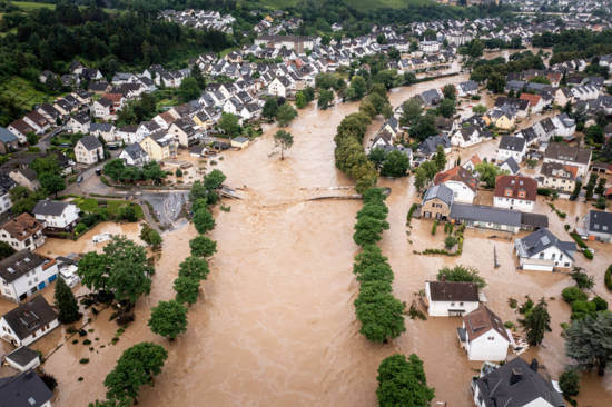 Überflutete Stadt - Häuser und Bäume entlang eines über die Ufer getretenen Flusses stehen unter Wasser.