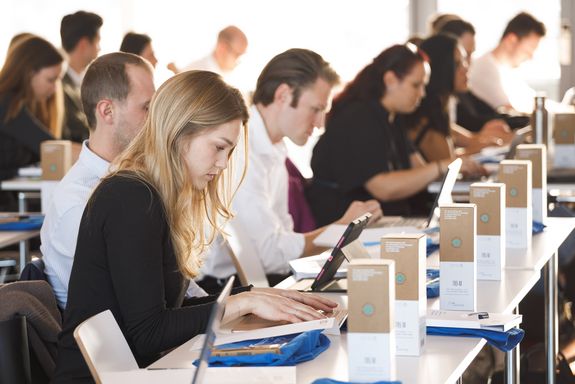 Studierende, die an Schreibtischen sitzen und in ihre Laptops sehen.