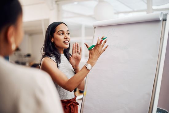 A woman standing in front of a flip chart talking to another person