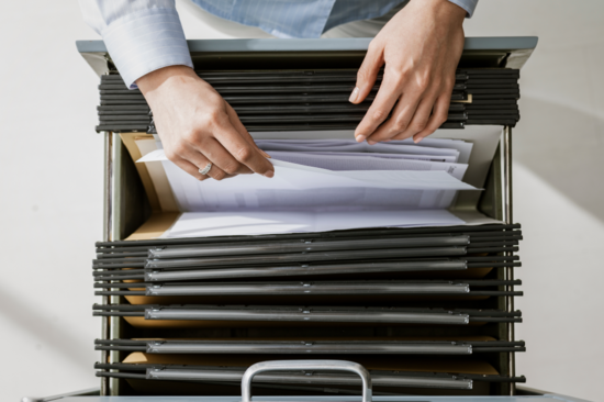 Perspective from above: a person reaches into the drawer of a filing cabinet and pulls out a sheet of paper.