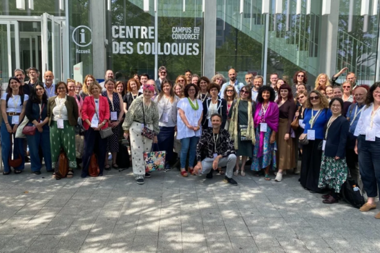 A group photo with about 50 people standing in front of the glass facade of a building with the inscription “Centre des Colloques.”