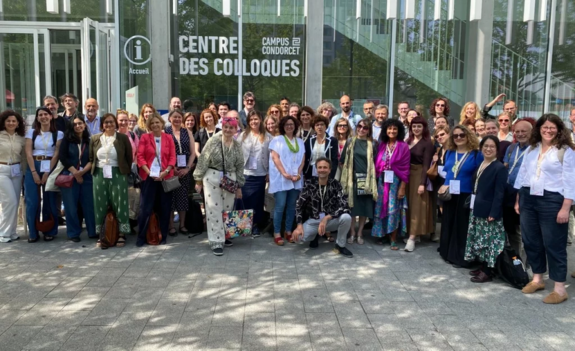 A group photo with about 50 people standing in front of the glass facade of a building with the inscription “Centre des Colloques.”