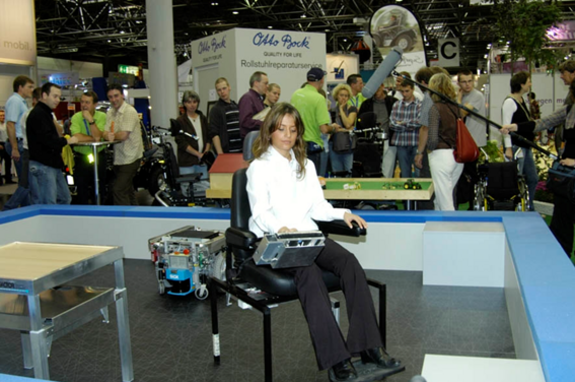 Vorführung auf der Rehacare Messe in Düsseldorf. Das Movement System ermöglicht vollautomatisches Docken des Sessels mit der daraufsitzenden Person und Transport an ein vorgewähltes Ziel. Die mobile Plattform kann im nächsten Schritt vom Sessel abkoppeln und den Tisch an eine Position, z.B. zur Person bringen. Eine Plattform kann mehrere BenutzerInnen und mehrere Module versorgen.