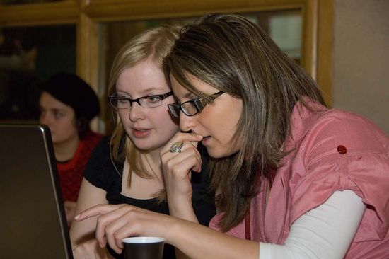 „Zwei junge Frauen arbeiten gemeinsam an einem Laptop und schauen konzentriert auf den Bildschirm.“
