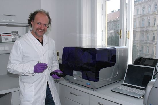 Prof. Andreas Farnleitner bei der Laborarbeit mit Proben in Pipetten und Pinzette in der Hand, neben ihm ein PCR-Gerät, dahinter ein Fenster.