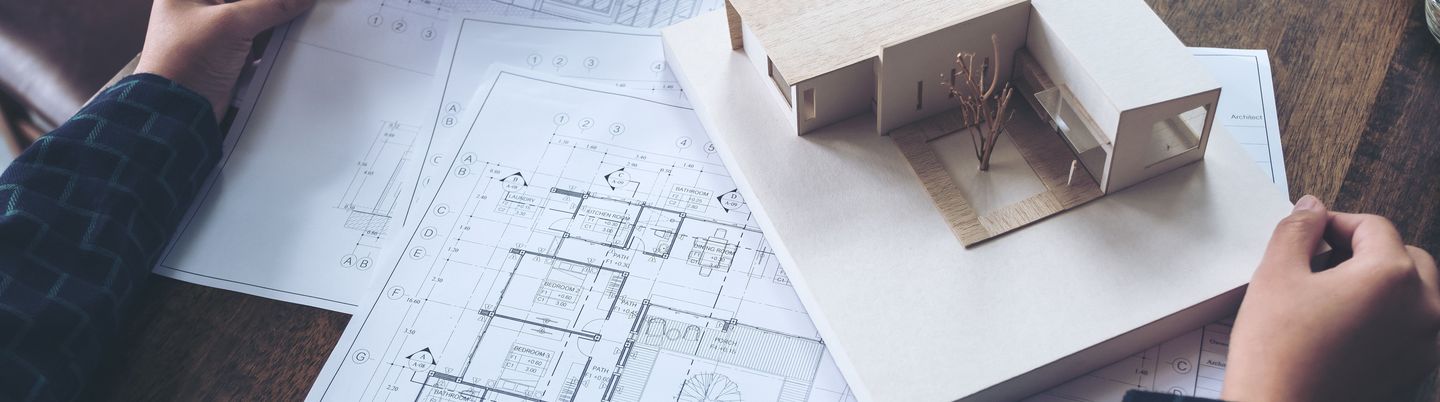 Ein Architekt, der an einem Architekturmodell mit Werkstattzeichnung auf einem Tisch arbeitet