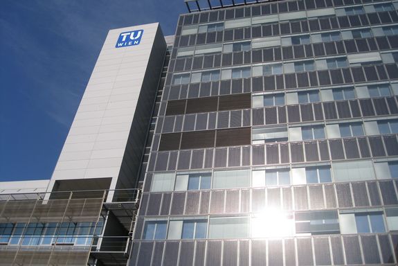 Frontalansicht: links ist ein Treppenhaus rechts ist das Hochhaus selbst. Beide Teile haben unterschiedliche Außenbild: Treppenhaus ist in eine graue Farbe ohne Öffnungen gehalten und das Hochhaus mit Glasfassade.