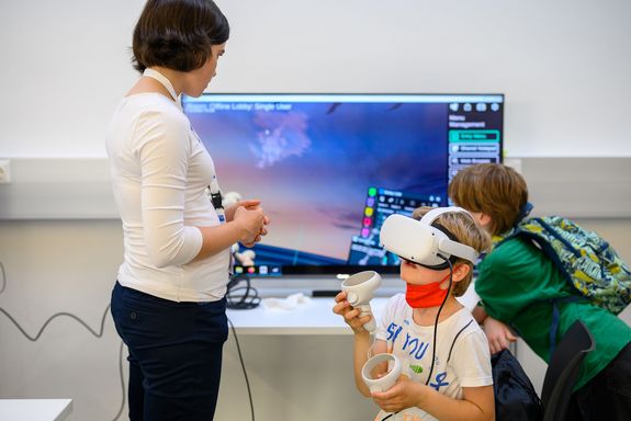 Kind mit VR-Headset, im Hintergrund ein großer Bildschirm.