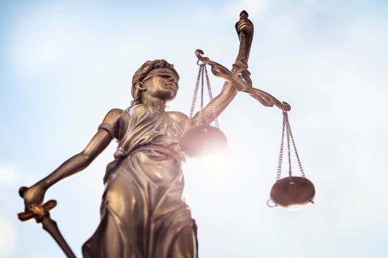 Eine Statue von Justitia von unten fotografiert, im Hintergrund blauer Himmel.