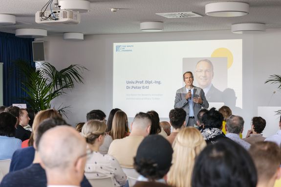 Mann mit Brille und Mikro auf Bühne in hellem Anzug