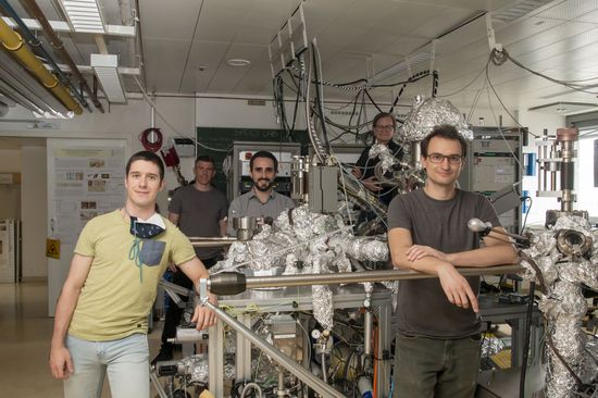 The 5-person team in a large research laboratory, all around a large vacuum system.