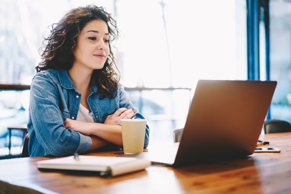  Young woman at a desk with laptop, coffee mug and notepad.