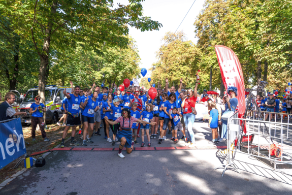Gruppe in der Prater Hauptallee mit TUW-T-Shirts. Davor ein Startband mit einer Clownin, die ihre Hände ausgebreitet hält.