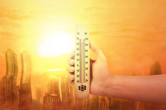 Hand hält heißes Thermometer, im Hintergrund sieht man eine flirrende Stadt.