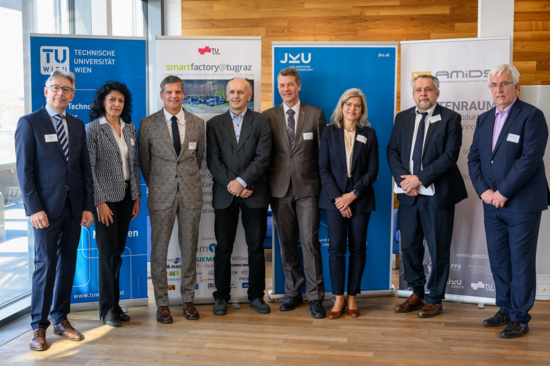 Gruppenfoto be der Kick_off Veranstaltung "Pilotfabriken" mit sieben Damen und Herren, im Business-Stil gekleidet. Hintergrund Roll-Ups der beteiligten Universitäten.