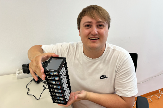 A male person sits at a desk and holds a block of eight mini-computers in his hands.