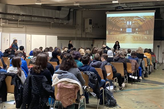 technik bewegt Begrüßung im Jahr 2022, Leinwand davor Sprecherin, Publikum sitzend von hinten fotografiert