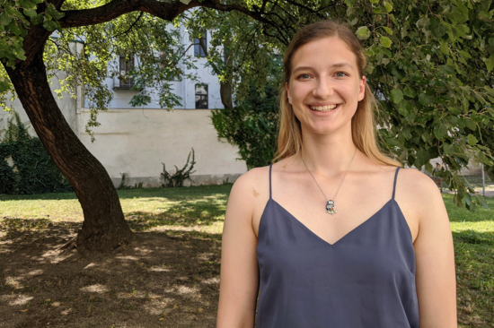 Porträtbild im Querformat von Marianne Röchling. Sie hat langes, glattes Haar und trägt ein Top. Im Hintergrund sind ein Baum und eine helle Mauer zu sehen.