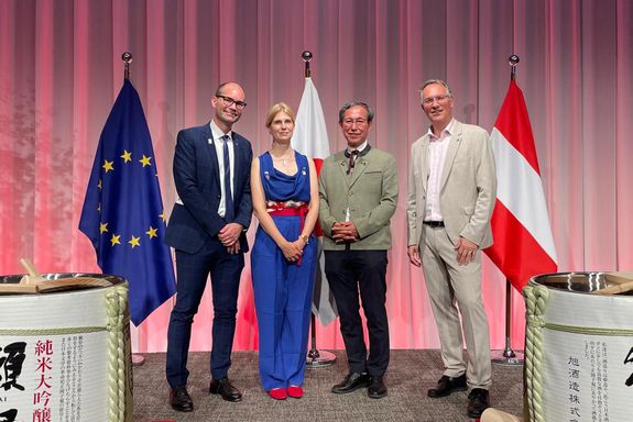 Drei Männer und eine Frau stehen neben einer Europa-, einer Japan- und einer Österreichfahne