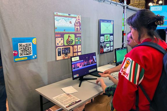 Kind sitzt am Computer und hebt die Hände über den Tisch.