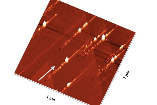 Nanostrukturen nach dem Ionenbeschuss: Der Pfeil zeigt die Richtung der Ionen an: Zunächst ensteht ein Graben mit Nanohillocks an beiden Seiten, ein besonders großer Hügel zeigt den Impakt-Punkt an, danach ist noch eine Erhebung entlang des Pfades zu sehen
