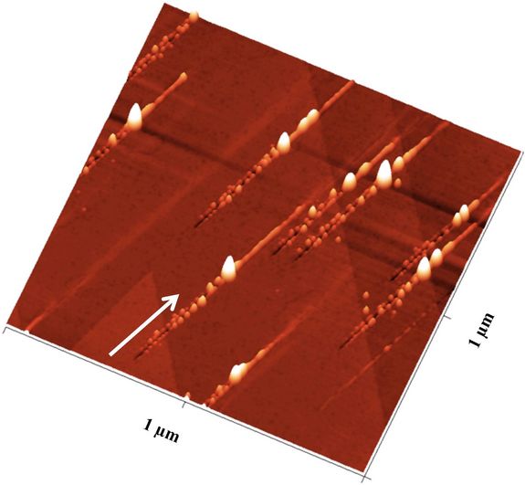 Nanostrukturen nach dem Ionenbeschuss: Der Pfeil zeigt die Richtung der Ionen an: Zunächst ensteht ein Graben mit Nanohillocks an beiden Seiten, ein besonders großer Hügel zeigt den Impakt-Punkt an, danach ist noch eine Erhebung entlang des Pfades zu sehen