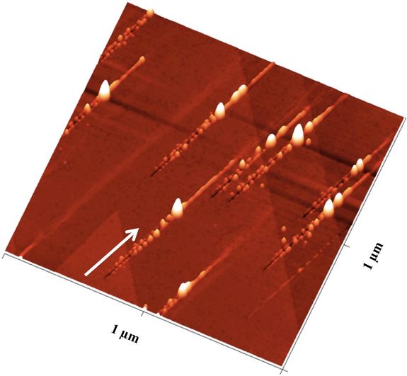 Nanostrukturen nach dem Ionenbeschuss: Der Pfeil zeigt die Richtung der Ionen an: Zunächst ensteht ein Graben mit Nanohillocks an beiden Seiten, ein besonders großer Hügel zeigt den Impakt-Punkt an, danach ist noch eine Erhebung entlang des Pfades zu sehen
