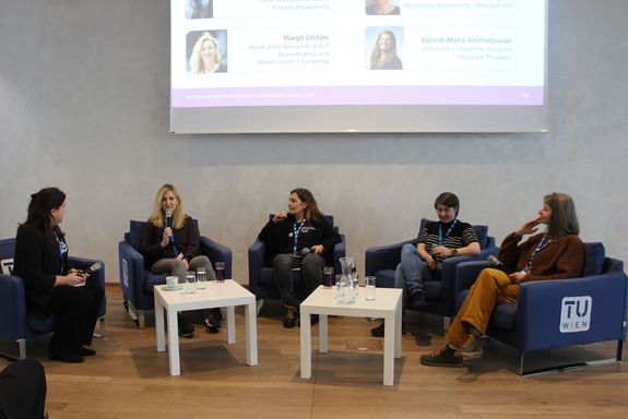 Vier Frauen auf Fauteuils vor einem Screen und zwei weißen Couchtischen