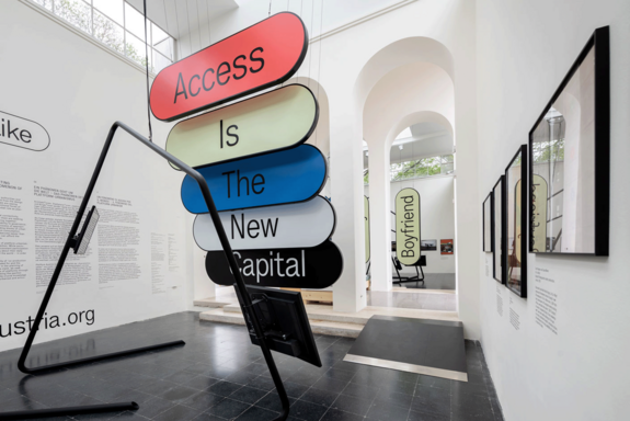 Raum im Österreich-Pavillon der Architekturbiennale Venedig mit bunten länglichen Schildern jeweils einem Wort: Access - is - The - New - Capital