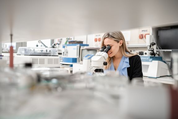 Forscherin sitzt im Labor und blickt durch ein Mikroskop 