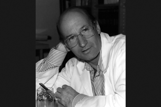 Prof. Mayer, auf seinen Schreibtisch gestützt, mit Labormantel, blickt direkt in die Kamera. S/w-Bild.