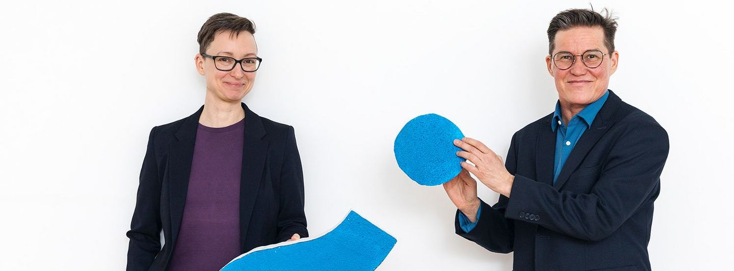 Teamfoto mit Marjo Rauhala und Bettina Enzenhofer, zwischen ihnen befindet sich ein großes Fragezeichen