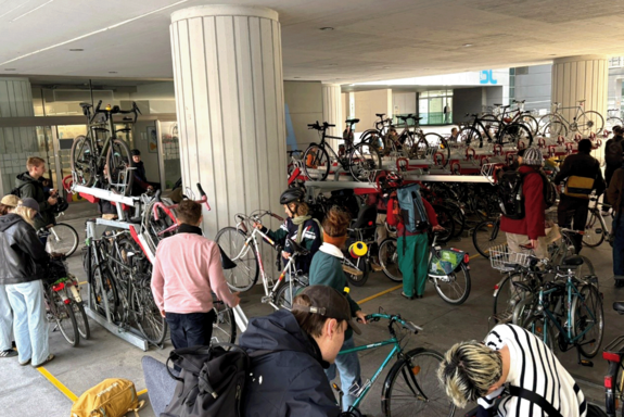 Personen mit ihren Fahrrädern beim Parken dieser. Sichtbar ist eine Fahrradparkmöglichkeit auf zwei Ebenen.