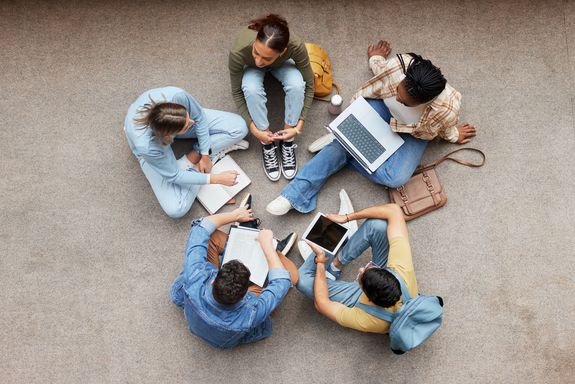 Studierende sitzen im Kreis am Boden mit Laptops, von oben fotografiert