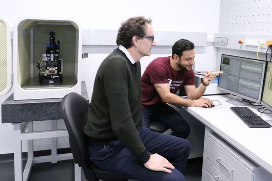 zwei Personen am Computer, dahinter ein Mikroskop