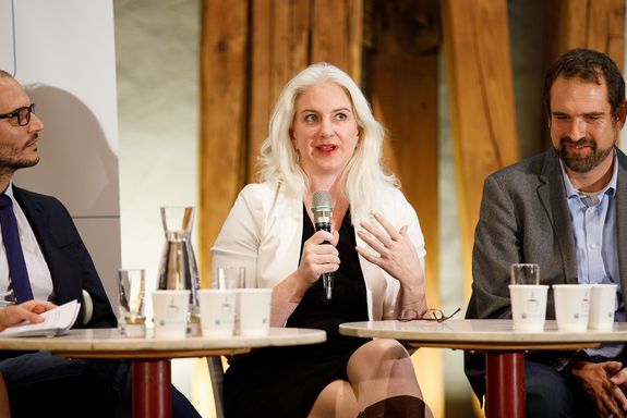Close up of Julie Rosser speaking into the microphone. Florian Rudroff can be seen on the left, Philipp Thurner on the right.
