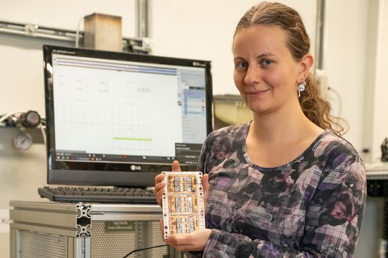 Woman holding an electronic control device, with a computer screen in the background. 