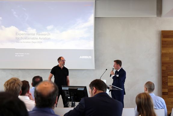 Zwei Männer stehen mit Mirkofon vor Leinwand
