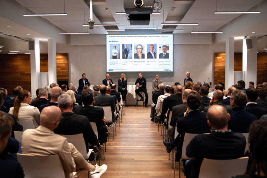 Voller Vortragsraum mit Blick auf mehrere Personen vor einem Screen.