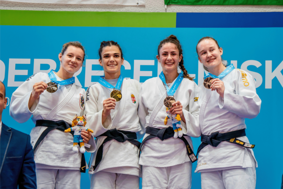 Vier Judoka im Anzug halten ihre Medaillen in Händen