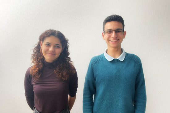 The photo shows a woman and a man standing in front of a white wall and smiling at the camera.